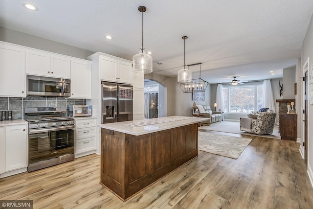 kitchen with arched walkways, white cabinets, appliances with stainless steel finishes, open floor plan, and backsplash