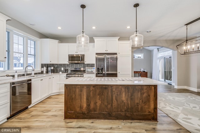 kitchen with arched walkways, stainless steel appliances, tasteful backsplash, light wood-style flooring, and a kitchen island