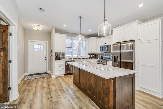 kitchen featuring light wood finished floors, tasteful backsplash, white cabinets, appliances with stainless steel finishes, and a sink