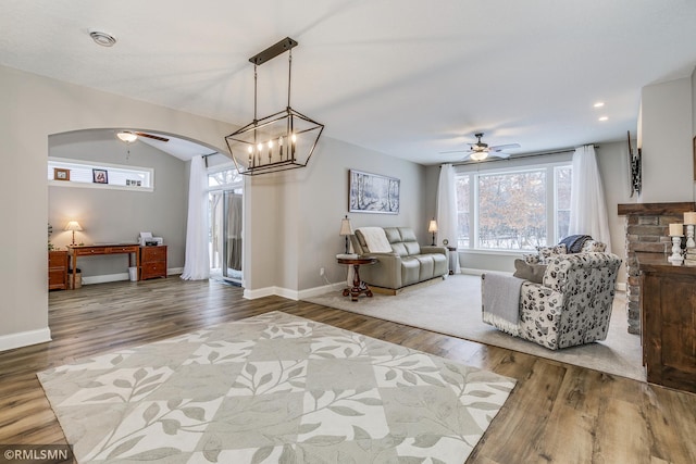 living area featuring a ceiling fan, baseboards, arched walkways, and wood finished floors