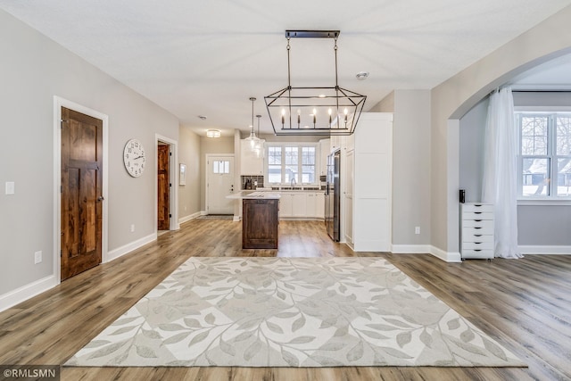 kitchen featuring arched walkways, white cabinetry, light wood-style floors, high end fridge, and a center island