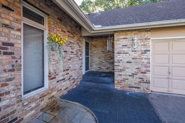 view of exterior entry with a garage, brick siding, and a shingled roof