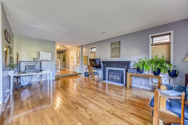 living area featuring a fireplace with flush hearth, baseboards, and hardwood / wood-style flooring