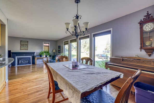 dining area featuring a textured ceiling, light wood-type flooring, a fireplace, and a notable chandelier