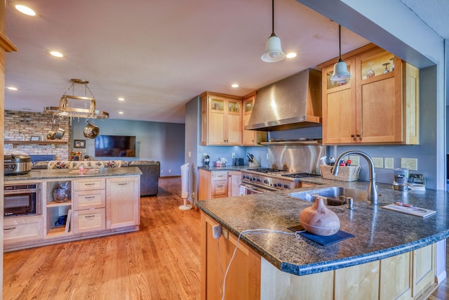 kitchen featuring high end range, open floor plan, a peninsula, wall chimney range hood, and a sink