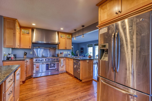 kitchen with stainless steel appliances, a peninsula, a sink, light wood-type flooring, and wall chimney exhaust hood