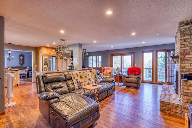 living area with a chandelier, a textured ceiling, light wood-style flooring, recessed lighting, and a brick fireplace