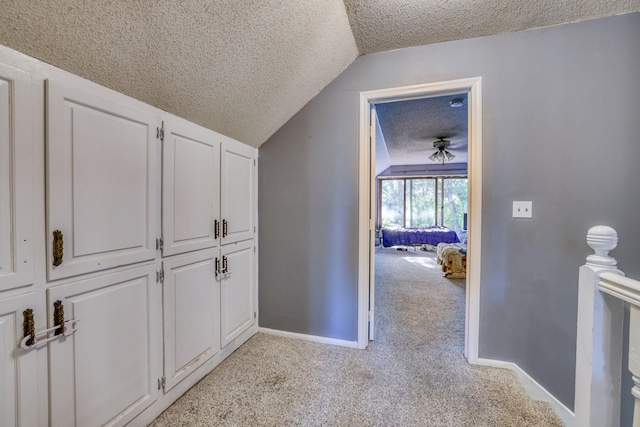 hall featuring light carpet, a textured ceiling, lofted ceiling, and baseboards