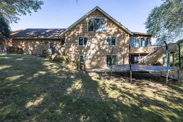 rear view of house with stairs, a deck, a trampoline, and a lawn