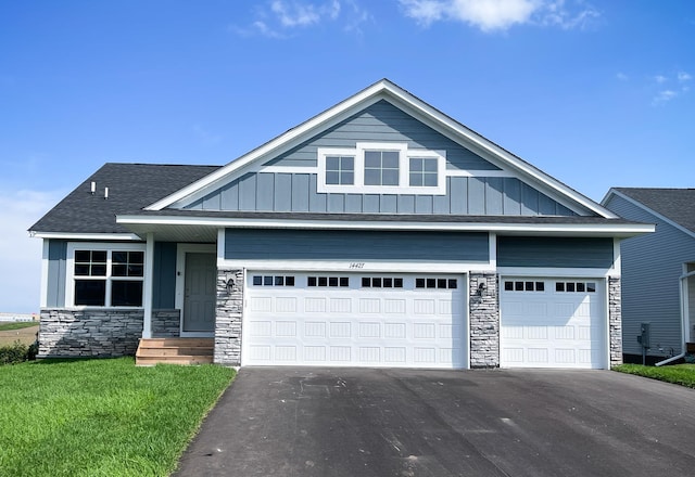 view of front of house with a shingled roof, stone siding, aphalt driveway, board and batten siding, and a front yard