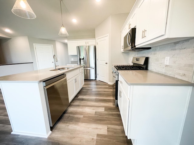 kitchen with stainless steel appliances, wood finished floors, a sink, white cabinetry, and backsplash