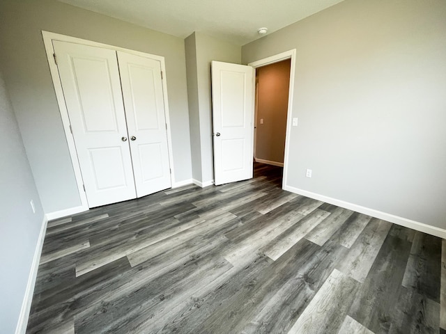 unfurnished bedroom featuring dark wood-style flooring, a closet, and baseboards