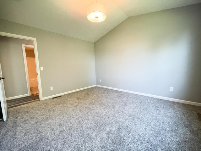 unfurnished room featuring baseboards, visible vents, vaulted ceiling, and carpet flooring