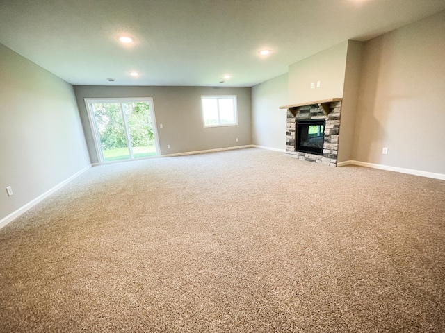 unfurnished living room with a stone fireplace, recessed lighting, carpet flooring, and baseboards