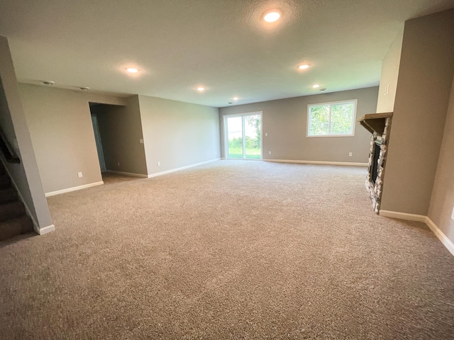 below grade area with light carpet, baseboards, stairs, a fireplace, and recessed lighting