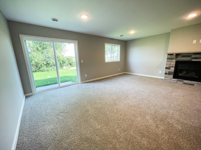 unfurnished living room with a stone fireplace, recessed lighting, carpet flooring, and baseboards