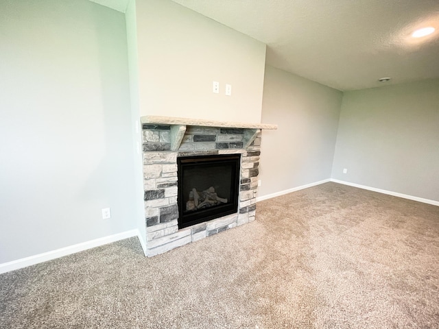 unfurnished living room with carpet flooring, a stone fireplace, and baseboards