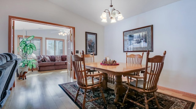 dining room featuring a notable chandelier, vaulted ceiling, baseboards, and wood finished floors