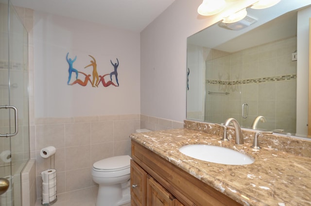 bathroom featuring vanity, a wainscoted wall, a shower stall, tile walls, and toilet