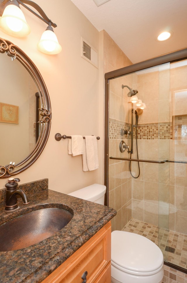 bathroom featuring visible vents, a stall shower, toilet, and vanity