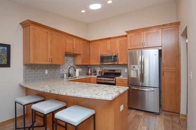 kitchen with a sink, backsplash, appliances with stainless steel finishes, a peninsula, and light wood finished floors