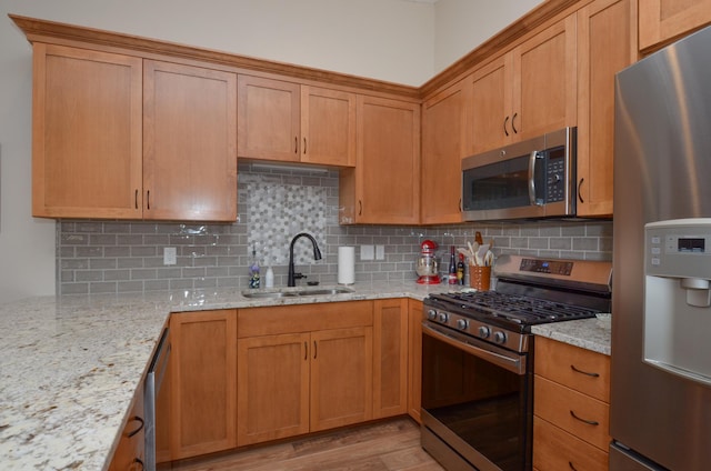 kitchen featuring decorative backsplash, light stone countertops, stainless steel appliances, and a sink