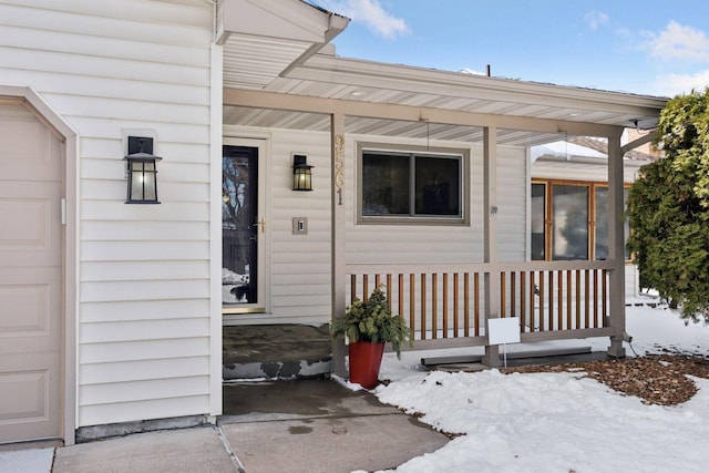 snow covered property entrance with a porch and a garage