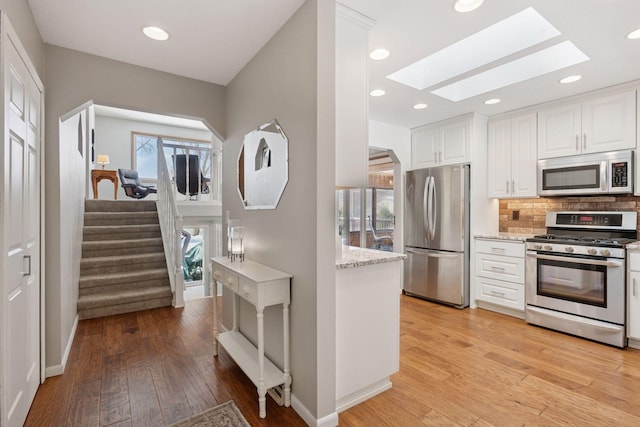 kitchen featuring a skylight, appliances with stainless steel finishes, white cabinetry, and tasteful backsplash