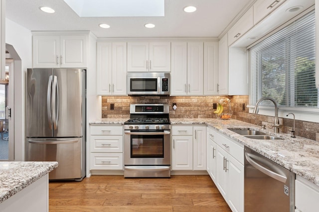 kitchen with light wood finished floors, a skylight, a sink, stainless steel appliances, and white cabinetry