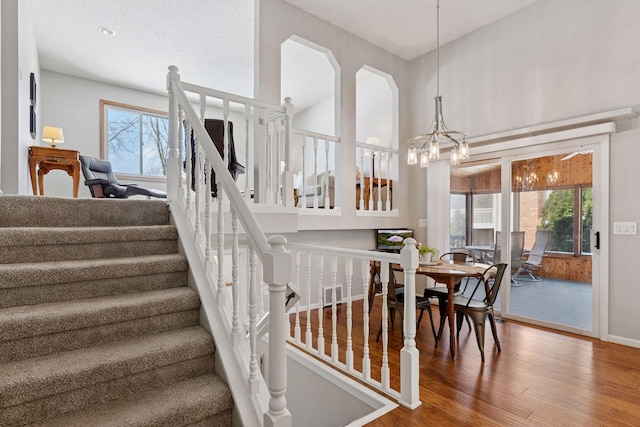 stairs with visible vents, plenty of natural light, a notable chandelier, and wood finished floors