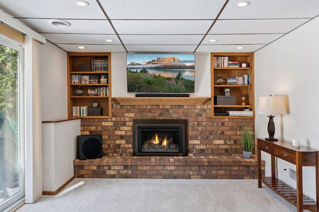 carpeted living room with baseboards, visible vents, built in shelves, and a brick fireplace