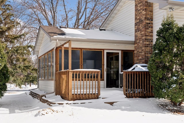 snow covered rear of property featuring a sunroom