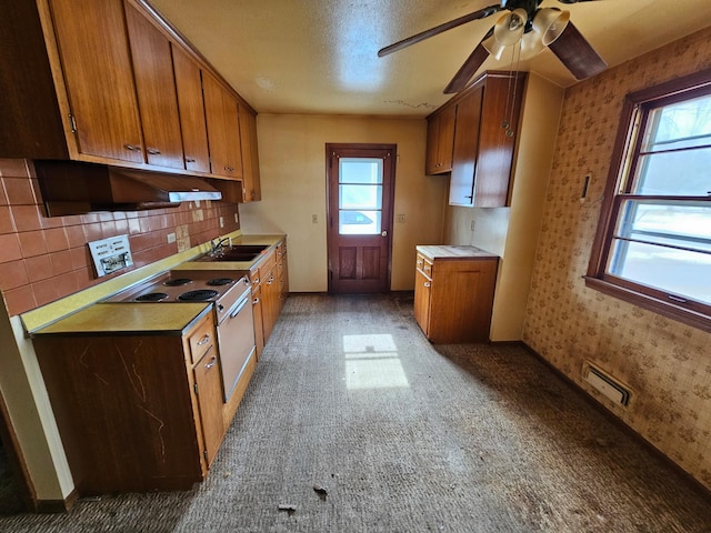 kitchen featuring tasteful backsplash, visible vents, brown cabinetry, a sink, and wallpapered walls