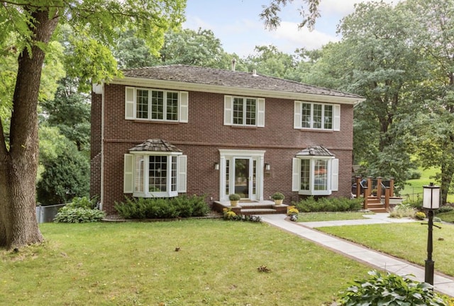 colonial inspired home with a front lawn, fence, and brick siding