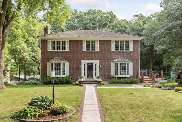 colonial house featuring brick siding, a chimney, and a front yard