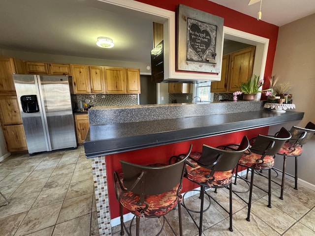 kitchen with a breakfast bar, tasteful backsplash, dark countertops, stainless steel fridge, and a peninsula