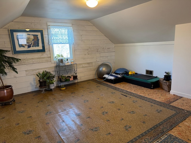 exercise area featuring visible vents, vaulted ceiling, and wood walls