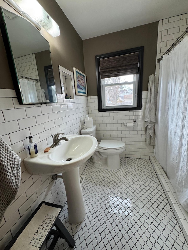 full bathroom with tile walls, toilet, wainscoting, a shower with curtain, and tile patterned floors