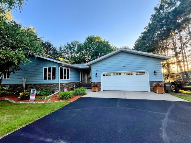 ranch-style house featuring stone siding, aphalt driveway, a front lawn, and an attached garage