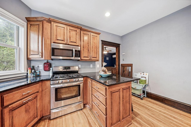 kitchen with dark stone countertops, a peninsula, light wood-style floors, appliances with stainless steel finishes, and brown cabinets