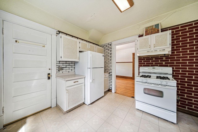 kitchen featuring under cabinet range hood, white appliances, brick wall, and light countertops