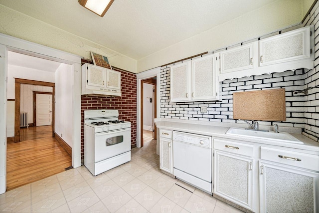 kitchen featuring radiator, light countertops, white cabinets, white appliances, and a sink