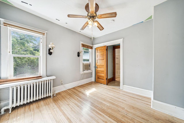 empty room with radiator, baseboards, light wood-type flooring, cooling unit, and a ceiling fan