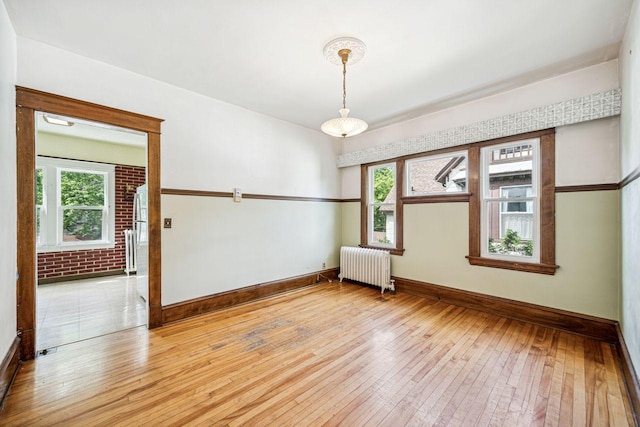 empty room with radiator, a healthy amount of sunlight, light wood-style flooring, and brick wall