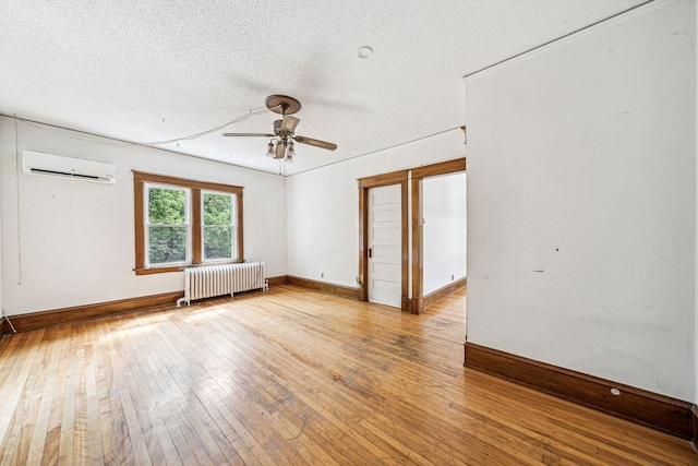 spare room with a wall mounted air conditioner, radiator, a textured ceiling, and hardwood / wood-style flooring