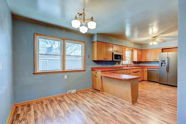 kitchen with appliances with stainless steel finishes, light wood-type flooring, a sink, and a peninsula