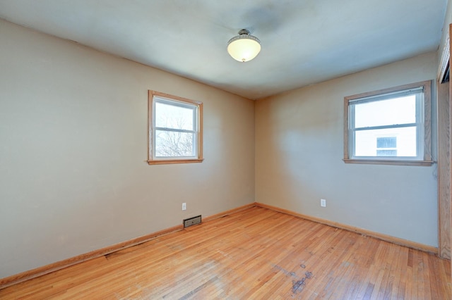 empty room featuring plenty of natural light, wood-type flooring, visible vents, and baseboards