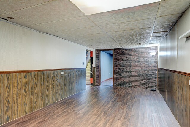 unfurnished room featuring a wainscoted wall, brick wall, wooden walls, and wood finished floors