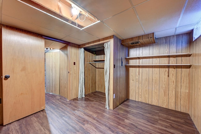 finished basement with wood walls, a drop ceiling, wood finished floors, and visible vents