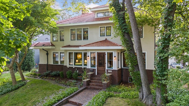 traditional style home featuring brick siding, a front yard, a tile roof, and stucco siding